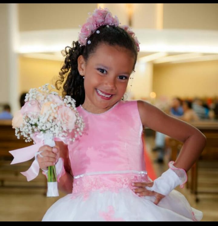 menina de 9 anos com vestido rosa e branco e um buque de fleres nas maos.